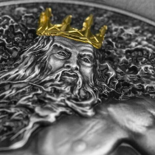 Gold crown on a detailed silver coin featuring a regal face, possibly a royal or mythological figure, with intricate engraved patterns and a textured background.