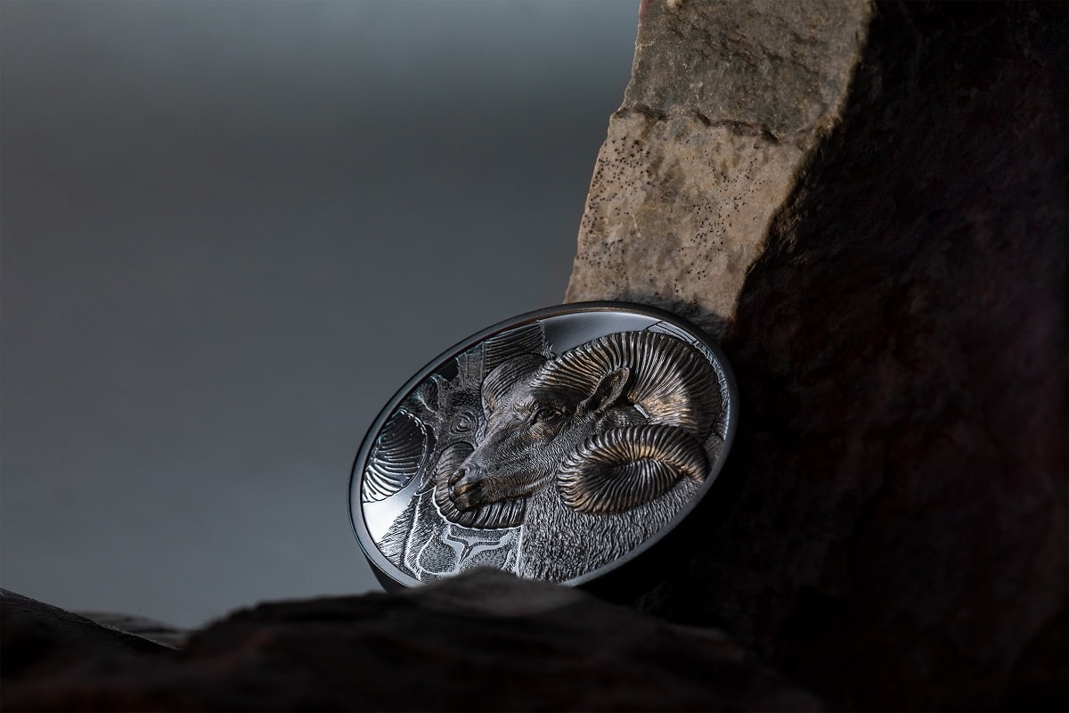 Silver collectible coin featuring detailed ram's head with intricate design, resting against a textured rock, showcasing craftsmanship and elegance for collectors.