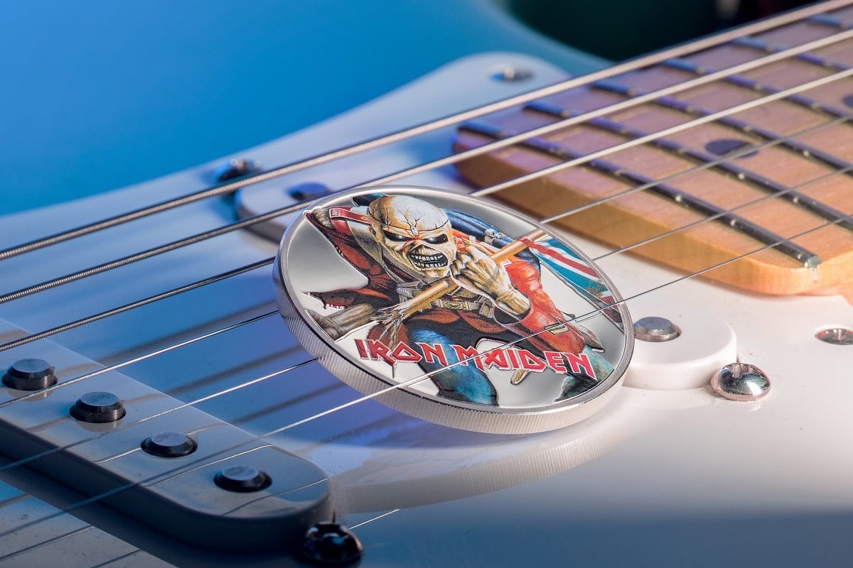 Iron Maiden collectible coin featuring the band's mascot, Eddie, on a guitar pick design, placed on an electric guitar. Perfect for music memorabilia collectors and fans of heavy metal.