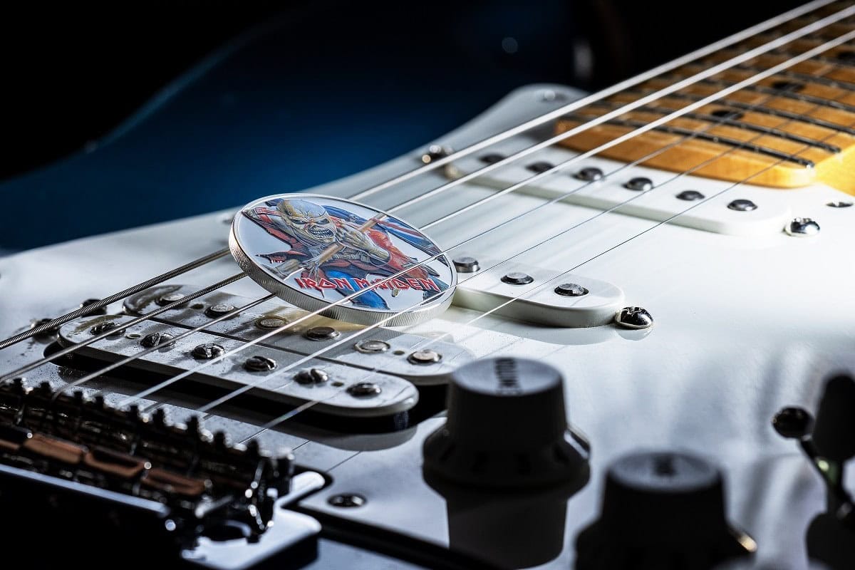 Vintage Iron Maiden guitar pick resting on electric guitar strings, showcasing classic rock memorabilia.