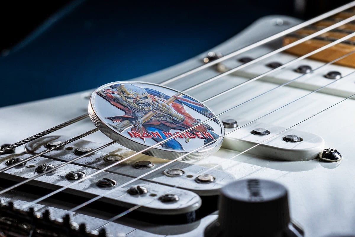 Iron Maiden band logo collector coin resting on electric guitar strings, showcasing a glossy finish and detailed artwork.