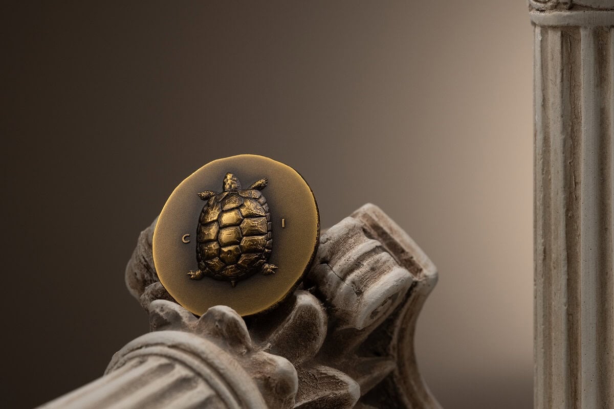 Gold-colored coin with turtle design, 2021, Greece collectible coin, detailed turtle engraving on smooth background, displayed on classical architectural column, fine craftsmanship, limited edition currency.
