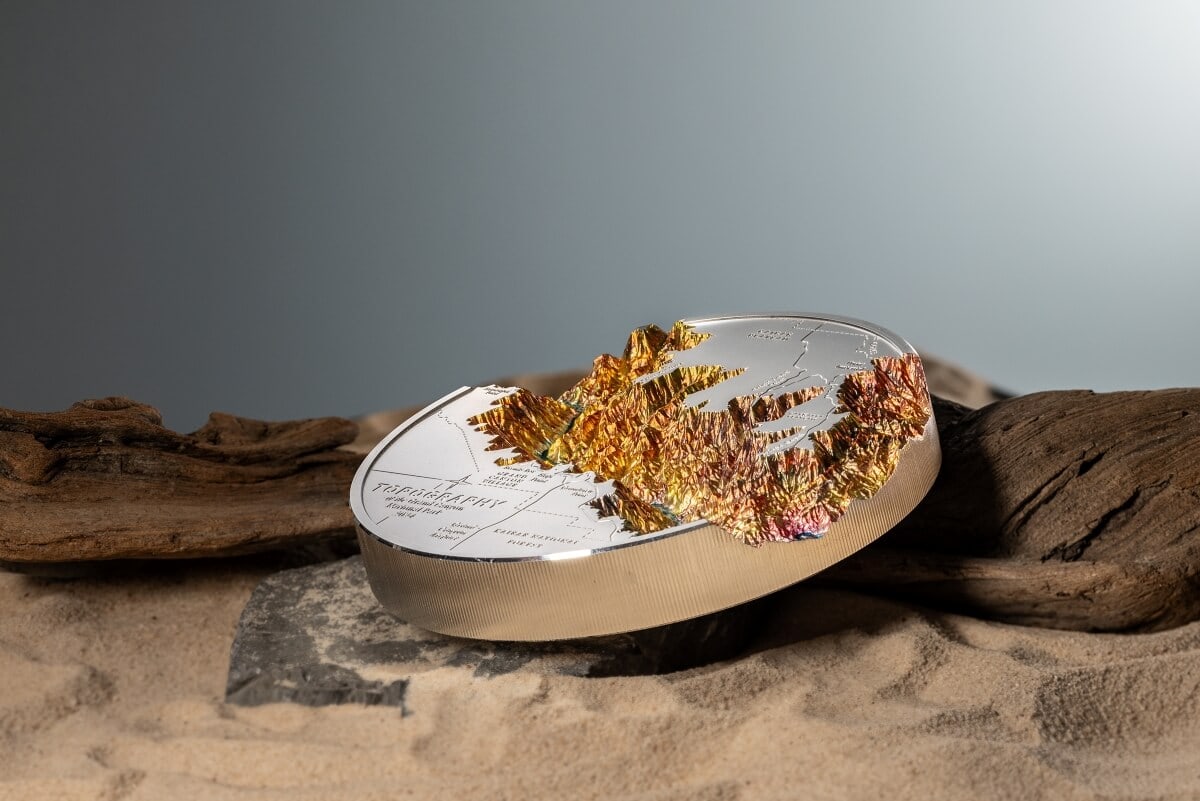 Golden mountain landscape on a commemorative coin, with intricate details and engraved map elements, set against a minimalist background for collectible coin display.