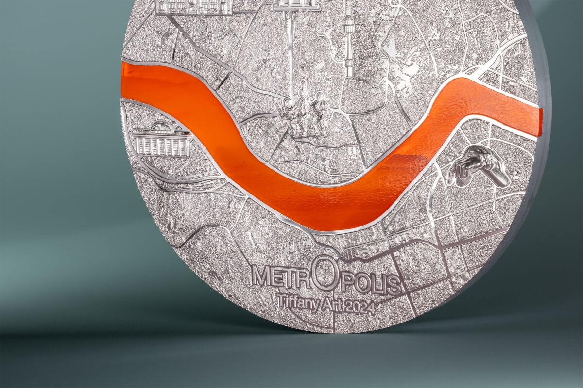 Silver collector coin featuring detailed city map, with orange enamel river accent, embossed "METROPOLE" text, and the artist name Tiffany An 2024.