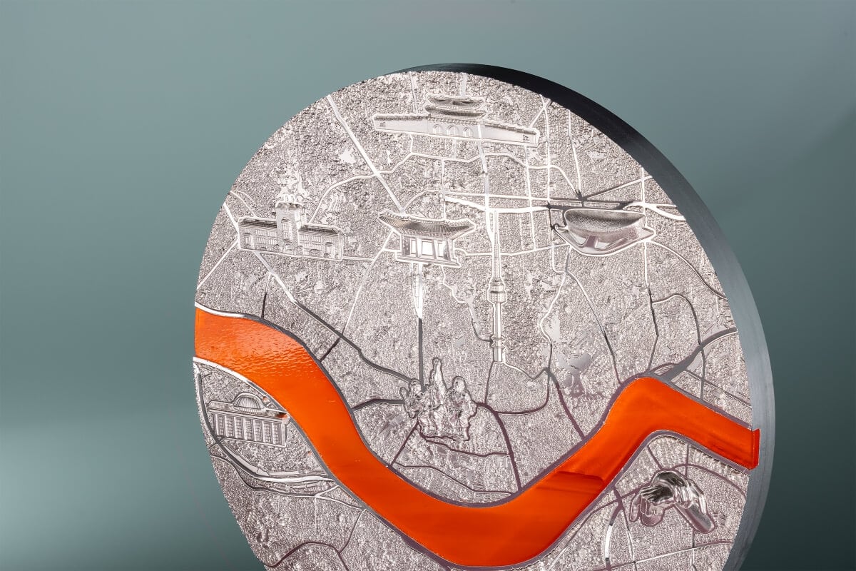 European city map coin with detailed landmarks, silver finish, and orange enamel accents.
