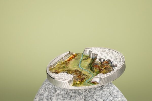 A 2024 Liechtenstein 100 Years of the Swiss Franc 1oz Silver Silk Finish Colorized Coin, standing upright on its edge on a light-colored, textured stone, with a blurred light green background.