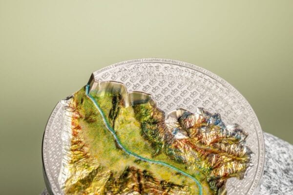 A 2024 Liechtenstein 100 Years of the Swiss Franc 1oz Silver Silk Finish Colorized Coin, displayed on a textured, light-colored surface resembling a basket weave, with a blurred light green background.