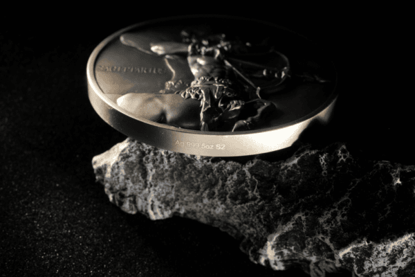 Antique silver bullion coin with detailed dragon design, inscribed with "Ag 999 5oz S2", resting on a textured rock against a black background.