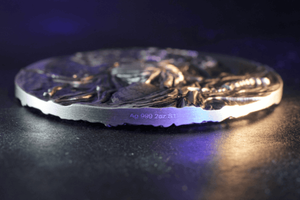 Precious metal coin featuring a detailed design, engraved with "Ag 999 2oz S1" indicating 2 ounces of 99.9% pure silver. A collectible item with a textured, artistic surface on a dark background.