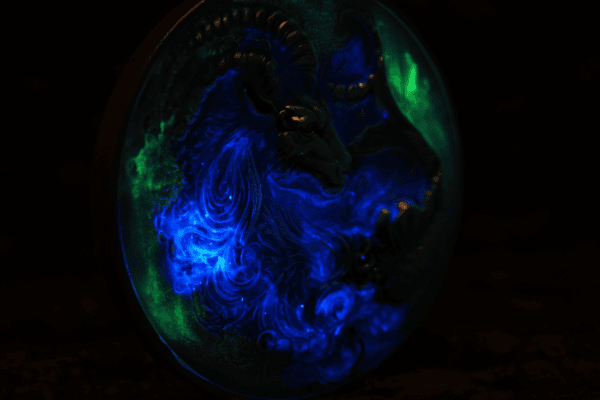 Glow-in-the-dark collectible coin featuring a detailed ram's head design, vibrant blue and green luminescence, dark background, intricate engraving, luminous details, and celestial themes, high-quality finish, limited edition.