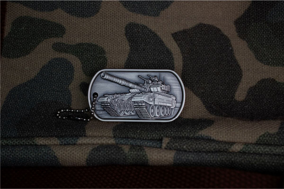 Dog tag with detailed tank illustration, military design, and camouflage fabric background.