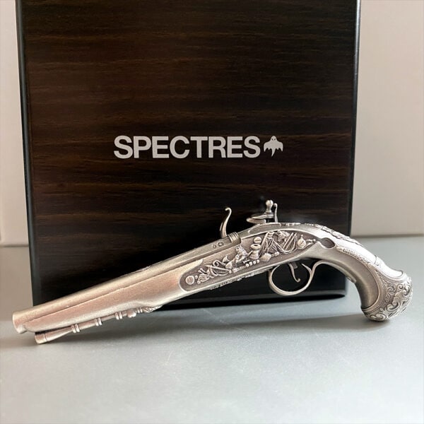 Silver ornate antique pistol with detailed engravings, placed in front of a dark wooden box labeled “SPECTRES”. Collectible historical firearm with intricate design, ideal for display or collectors.