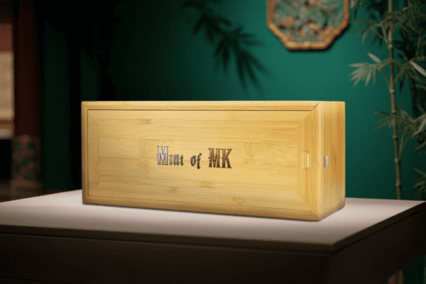 Wooden presentation box for the 2024 Chad “A Thousand Li of Rivers and Mountains” Coin with title engraved on lid; box rests on a green-toned surface with natural accents including plant elements.