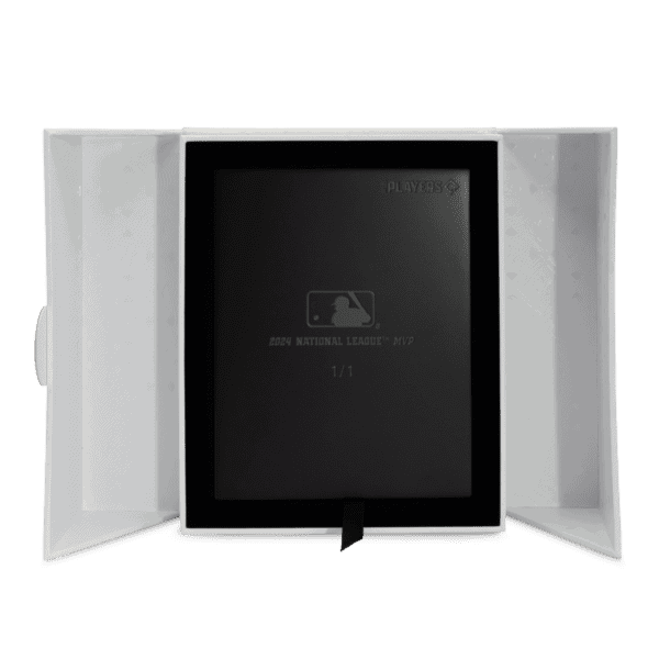 A black collector's box with a logo on the lid, sitting open inside a white cardboard sleeve. The black box is revealed to be a trading coin set.