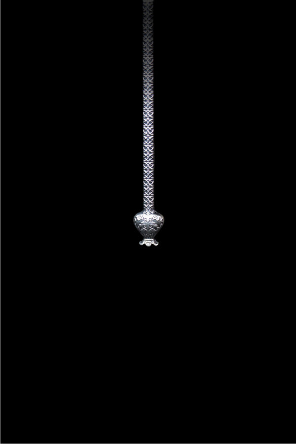 A close-up, bottom-up image of the lower part of a silver, antiqued medal in the shape of a winged staff, focusing on a spherical orb at its base.