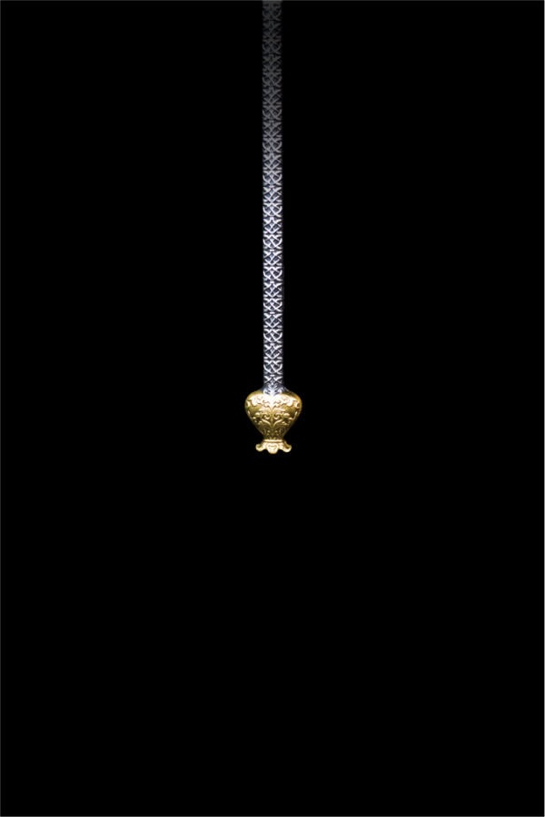 A close-up back view of the bottom tip of a gilded staff.