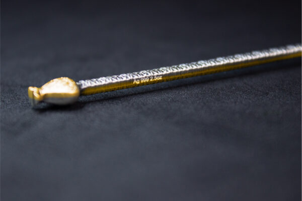 A close-up side view of the bottom of a gilded staff, showing the detailed inscription on its surface.
