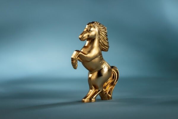 A gilded, silver coin shaped like a horse rearing on its hind legs, viewed from the side and slightly from the back.