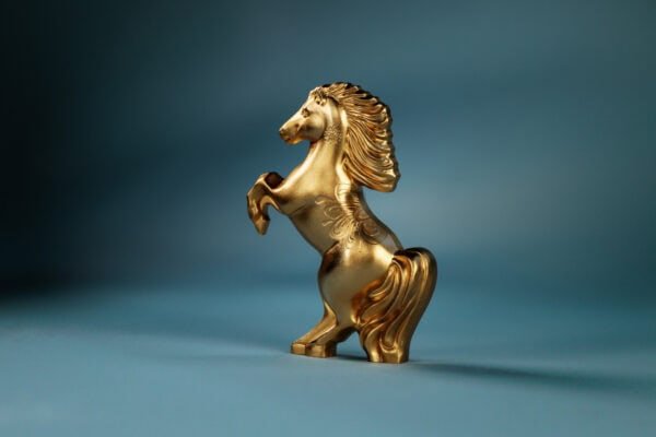 A gilded, silver coin shaped like a horse rearing on its hind legs, viewed from the side.