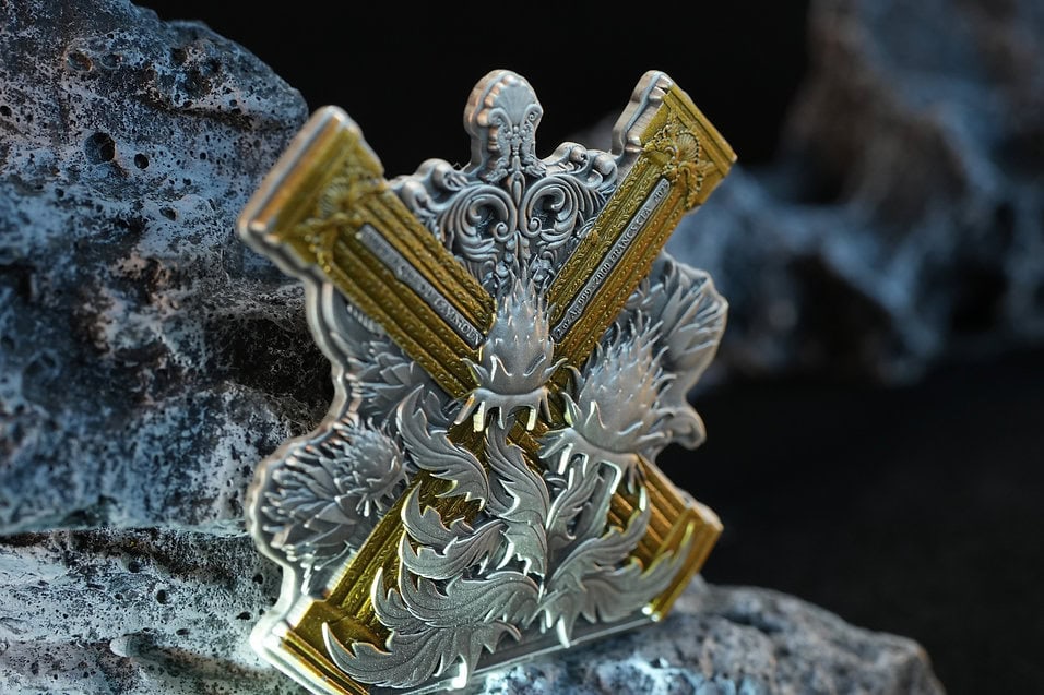 Gold and silver collectible coin with intricate dragon design, placed on rocks.