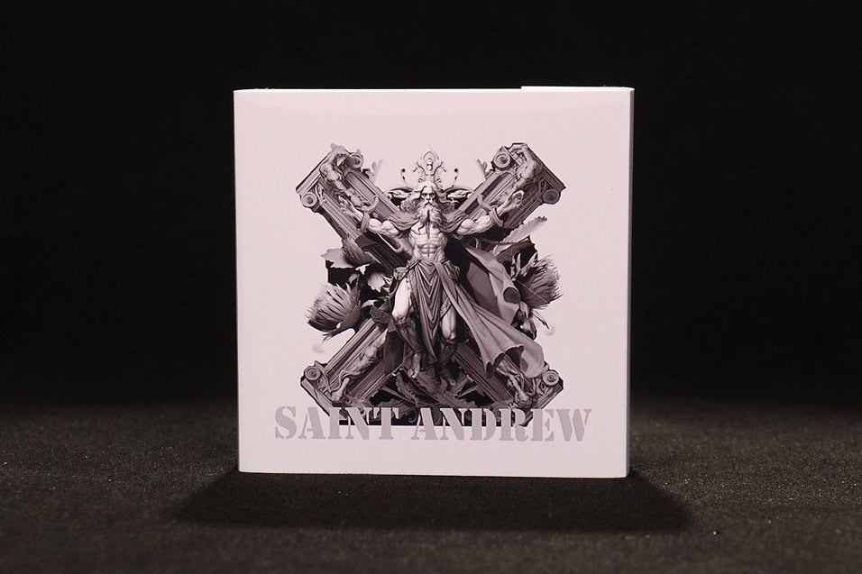 Saint Andrew collectible coin packaging featuring a detailed illustration of the saint crucified on a cross, with intricate design elements and the text "SAINT ANDREW" at the bottom.