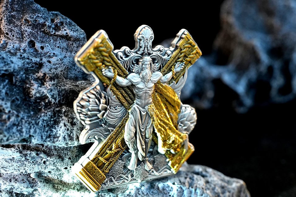 Antique silver and gold religious medal featuring Jesus Christ carrying a cross, intricately detailed and set against a rugged stone background.