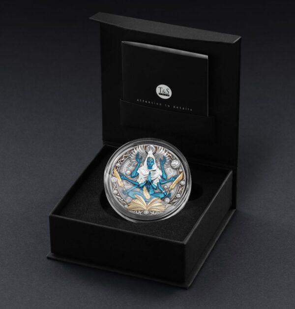 An open black presentation box reveals a coin with a multi-armed blue figure and gilded elements. The box is made of a matte material with a soft interior.