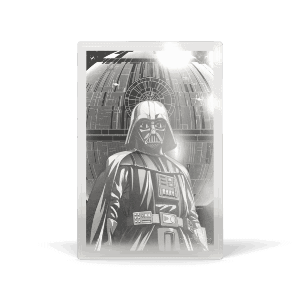 A silver proof foil featuring Darth Vader in a black and white image. He is standing in the foreground, facing forward with a slight tilt to the right. He is in full armor, with his helmet on and his cape flowing behind him. The background is a blurry, dark image of a Death Star interior. The image has a metallic sheen and looks like a collectible coin or foil.