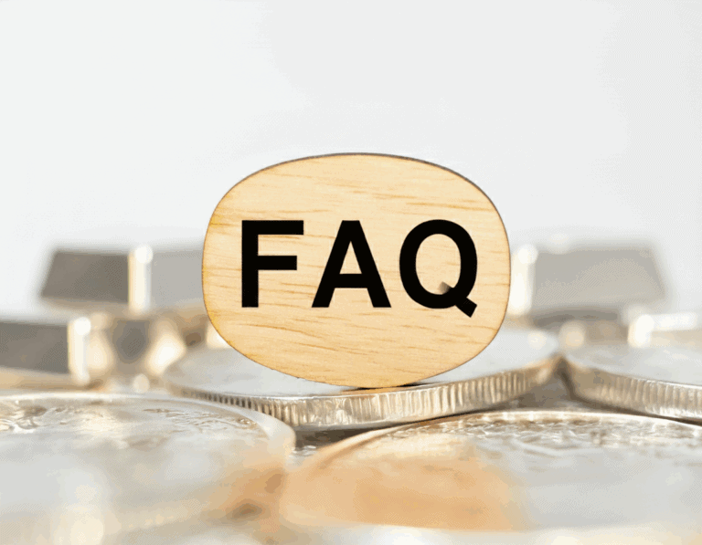 A close-up shot of a wooden block with the letters "FAQ" on it. In the background, out of focus, a stack of silver coins and a larger silver bullion bar are visible, suggesting frequently asked questions about silver.