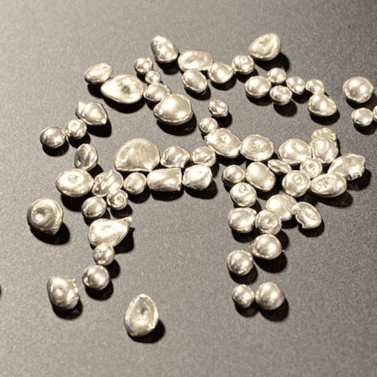 Rough angle view of baroque white pearls scattered on a dark surface, showcasing their irregular shapes and luster.