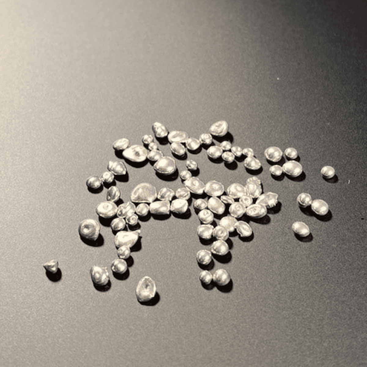 Shimmering white pearls scattered on a dark surface, showcasing their lustrous surface and unique irregular shapes.