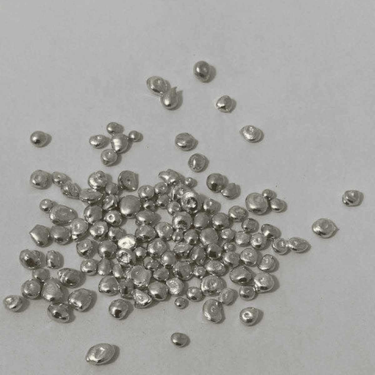 Tiny silver beads spread out on a flat gray surface, capturing their reflective surfaces and small, rounded shapes.