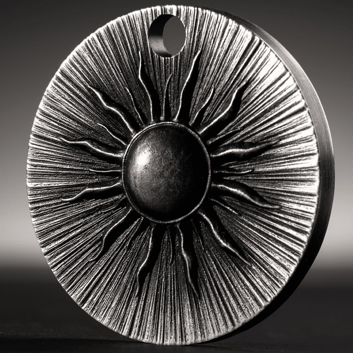 The image shows a close-up of a silver coin with a sun motif, emphasizing its detailed design and antiqued finish.