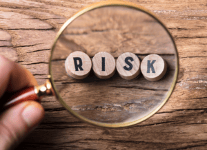 Risk_gr_reserve image: Magnified view of the word "RISK" spelled with wooden blocks, viewed through a magnifying gl.