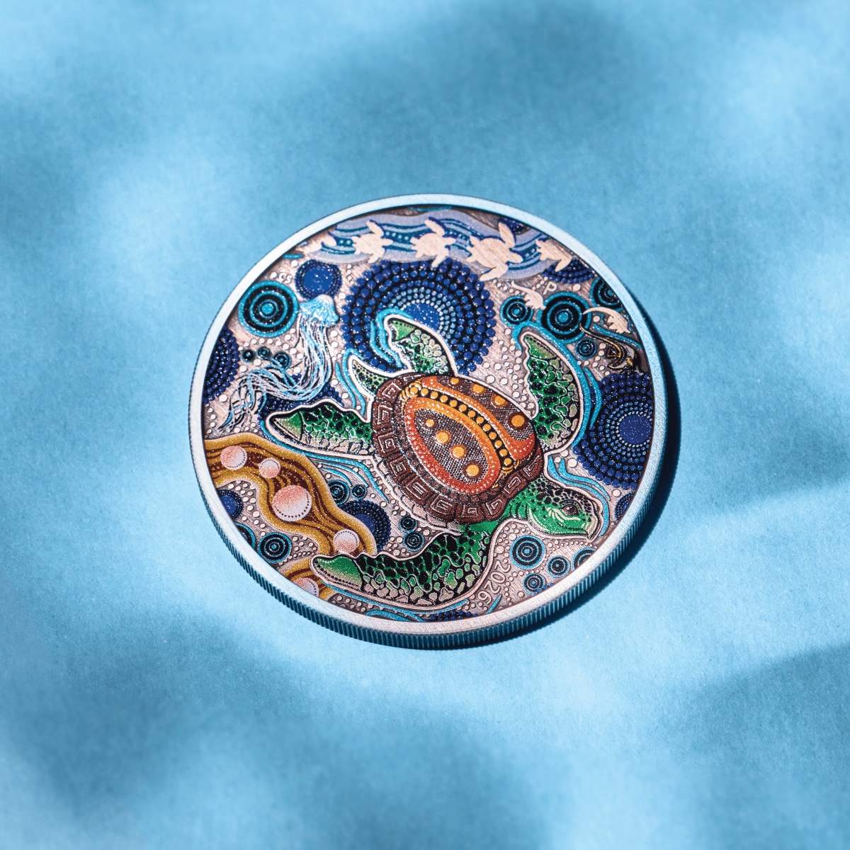 Turtle Yaunati antiqued coin resting on blue fabric, its colorized Aboriginal turtle reverse lit.