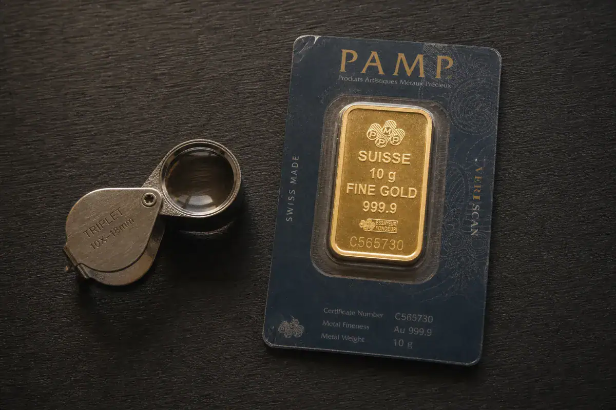 PAMP Suisse gold bar in assay card beside jeweler's loupe showing hallmark and serial number