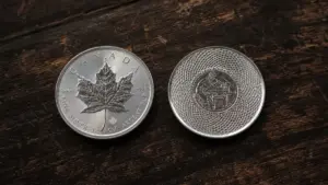 Sovereign coin and private mint silver round side by side on dark walnut, showing mint mark details